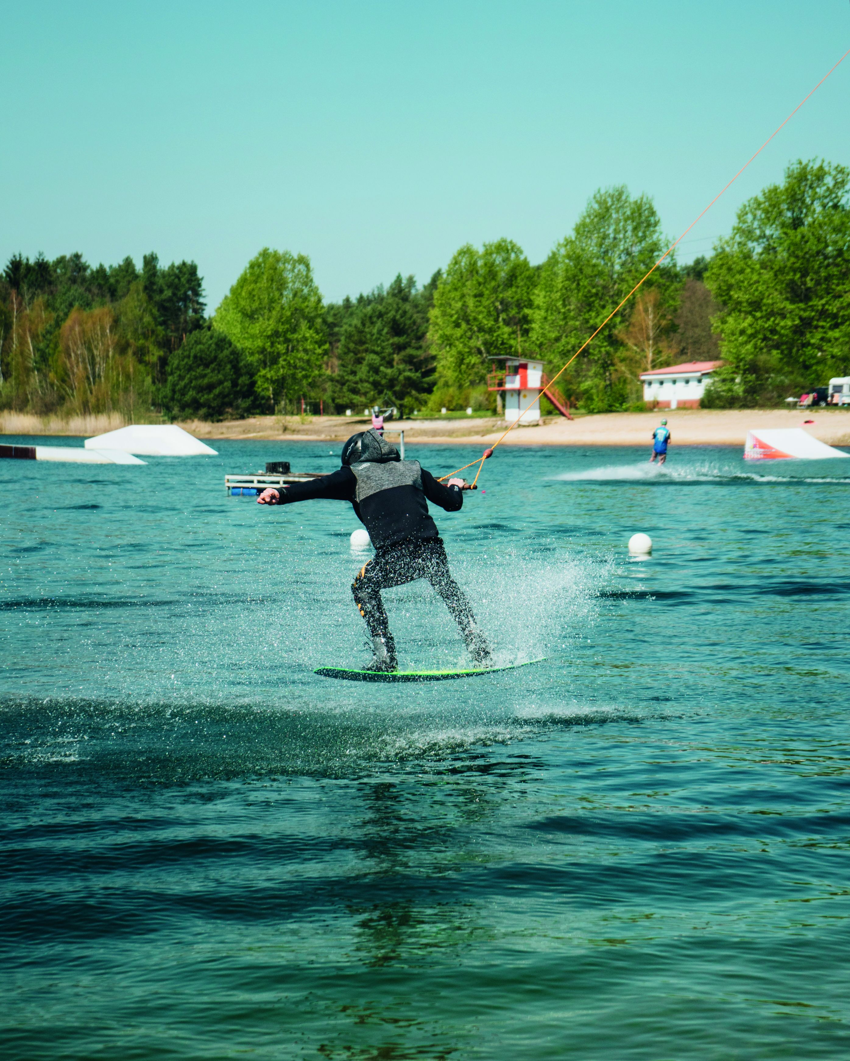 Iemand doet aan wakeboarden op een waterlichaam, met een heldere lucht en bomen op de achtergrond.