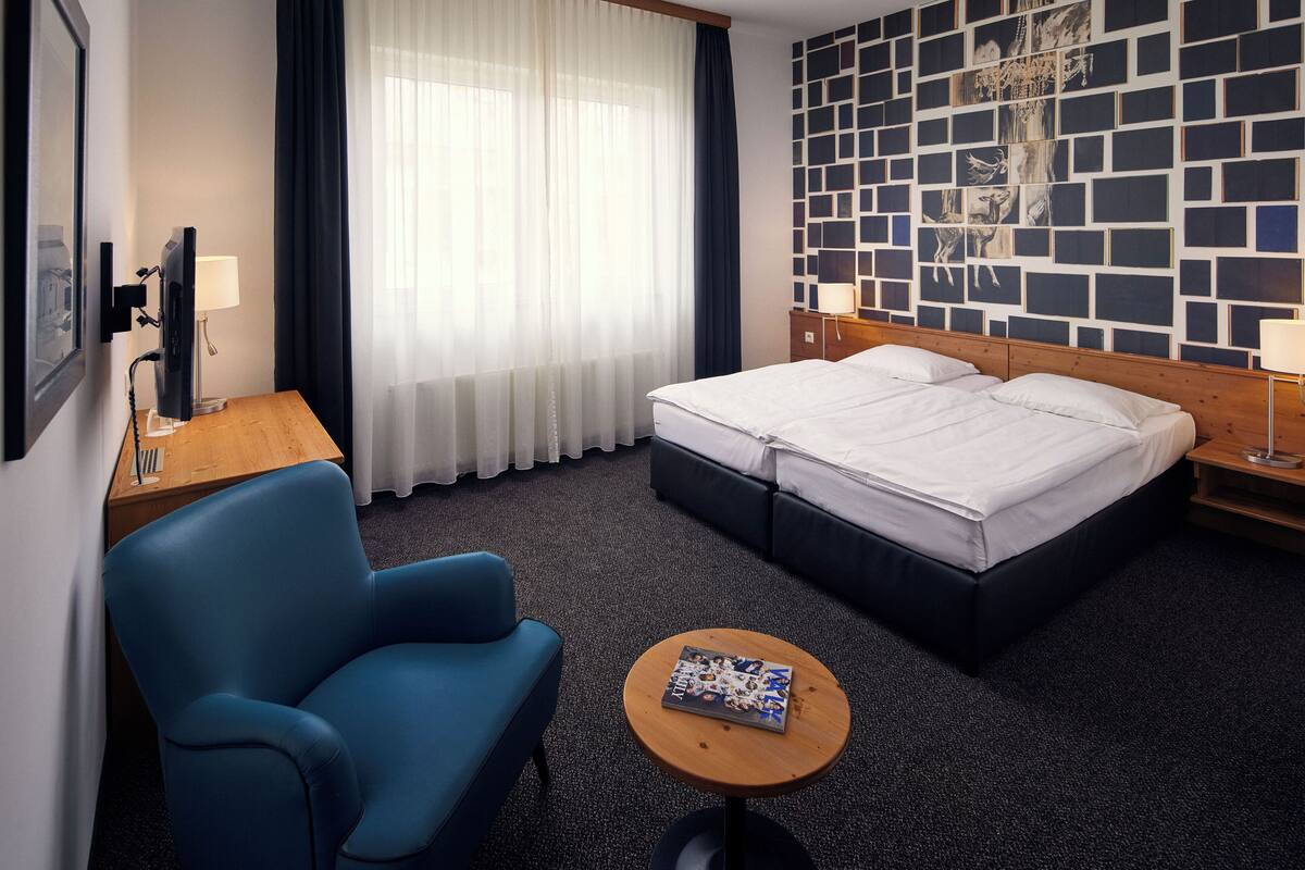 Ein Hotelzimmer mit Bett, Schreibtisch, Stuhl, kleinem Tisch und Wand mit geometrischem Muster.