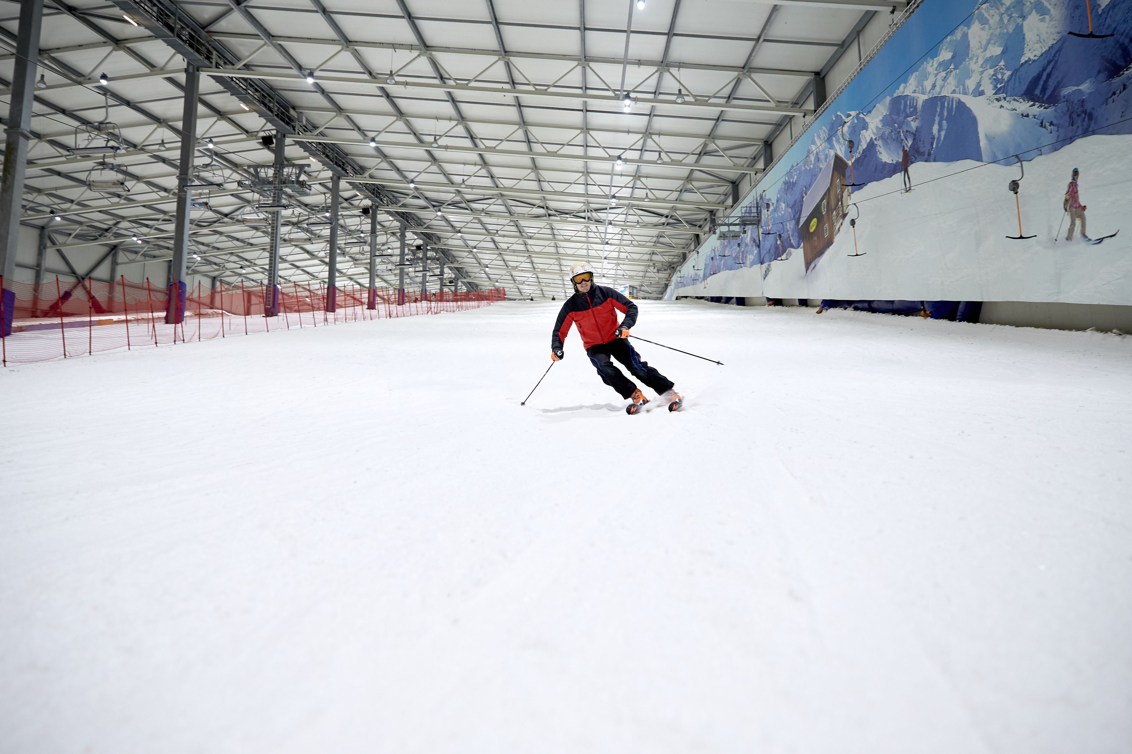 An indoor skiing facility with a high ceiling and snow-covered floor.
