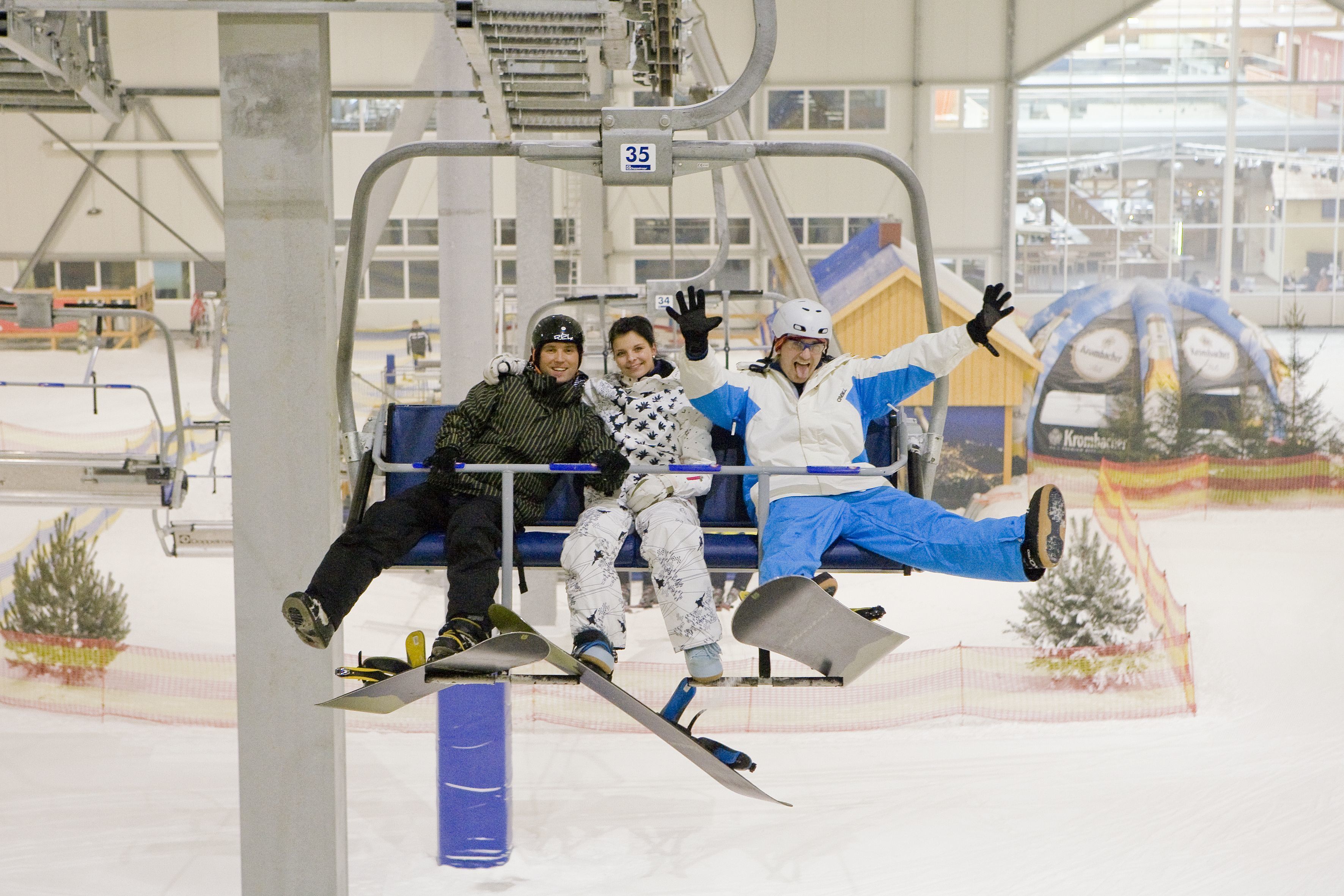 A ski lift with three people posing on the bar.