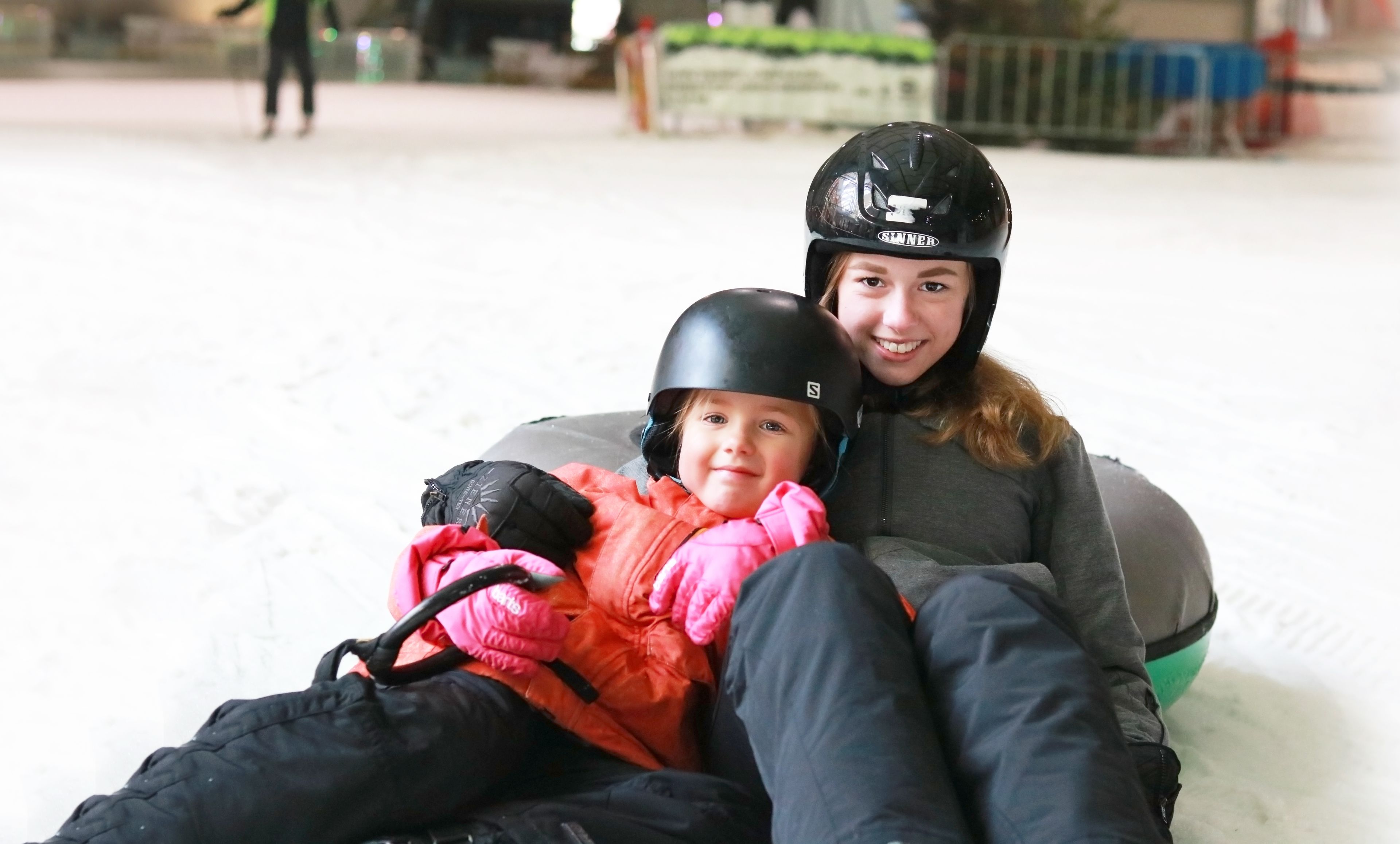 A person sitting on a sled with a helmet, wearing a jacket and pants.