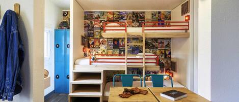 A bunk bed with a wall of travel posters, a wooden table with a book and sunglasses, and a blue chair.