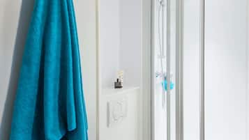 Une salle de bain avec une douche à parois de verre, un porte-serviettes avec une serviette bleue et une petite étagère contenant des articles de toilette.