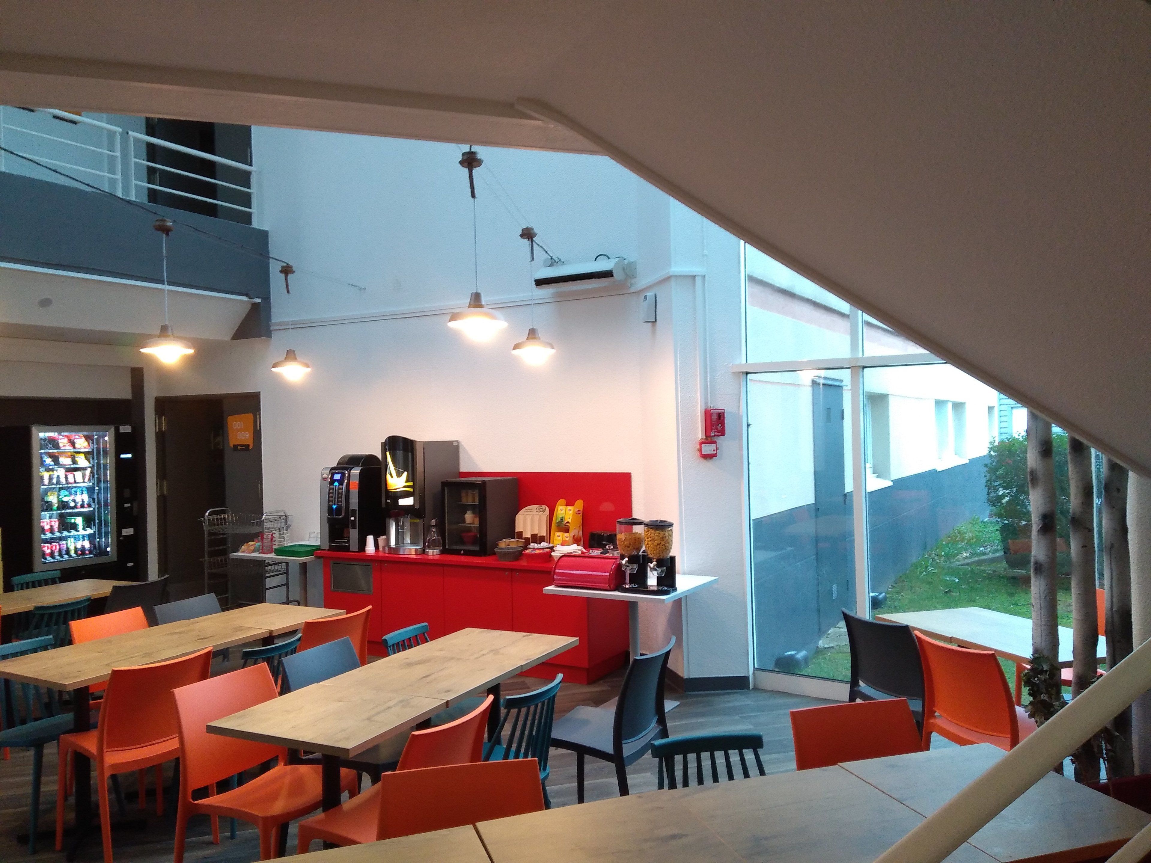 Ein modernes Café mit einer roten Theke, mehreren Tischen und Stühlen.