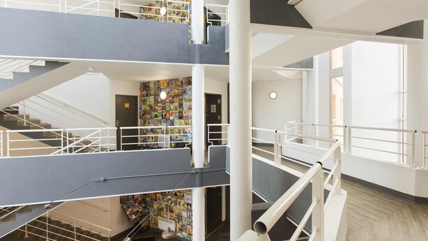 A multi-level interior with a central column, white railings, and a colorful wall mural. - hotelF1 Maurepas (Maurepas)