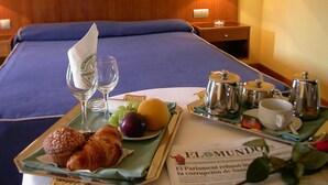 A hotel room with a neatly made breakfast tray, a bed with blue bedding, and a lamp on the nightstand.