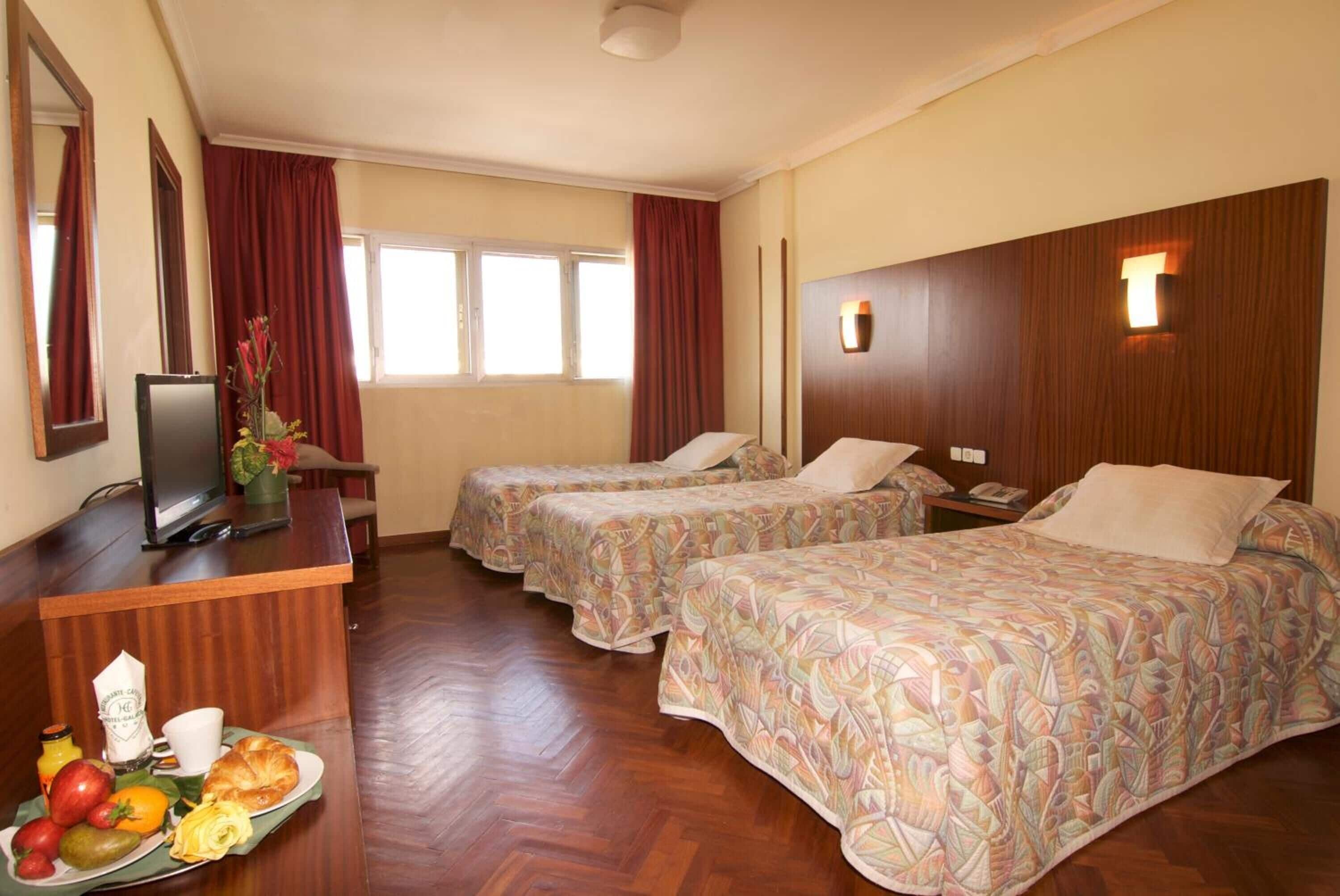 A hotel room with two beds, a desk with a television, and a breakfast tray.