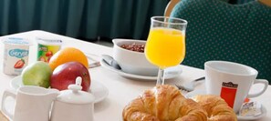 Une table dressée pour le petit-déjeuner avec un croissant, des fruits, du jus et du café.