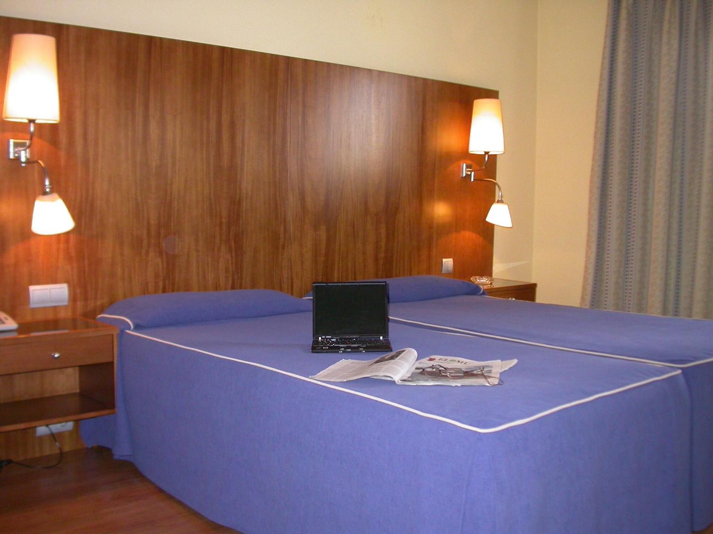 Una habitación de hotel con una cama grande, una laptop sobre la cama y dos lámparas de noche.