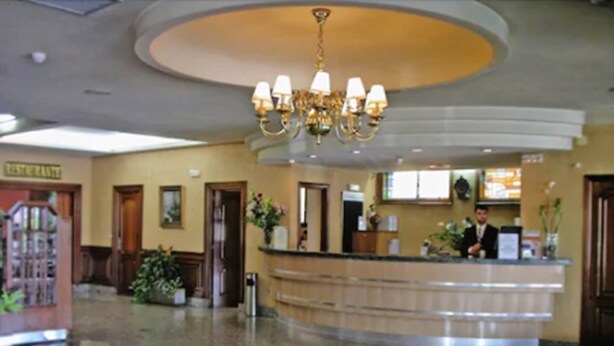 A hotel lobby with a reception desk, a chandelier, and a floor design.