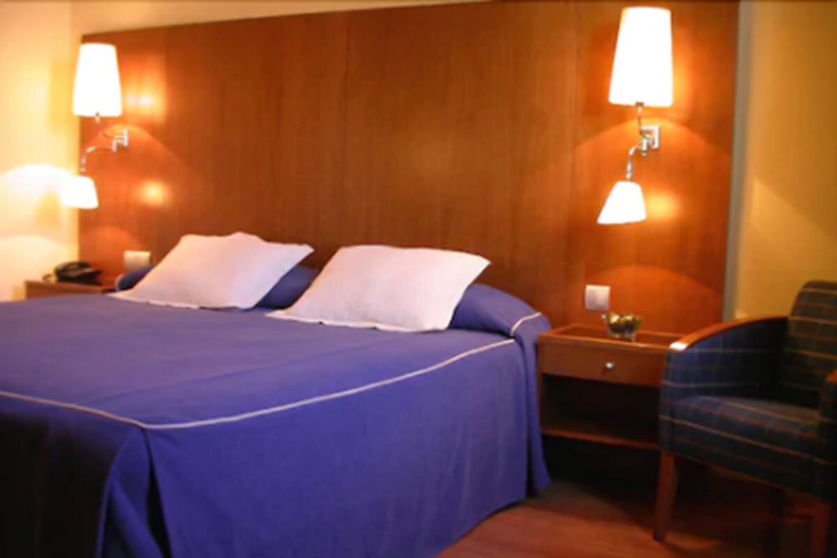 Una habitación de hotel con una cama grande, dos lámparas de noche, una mesita de noche y una silla.