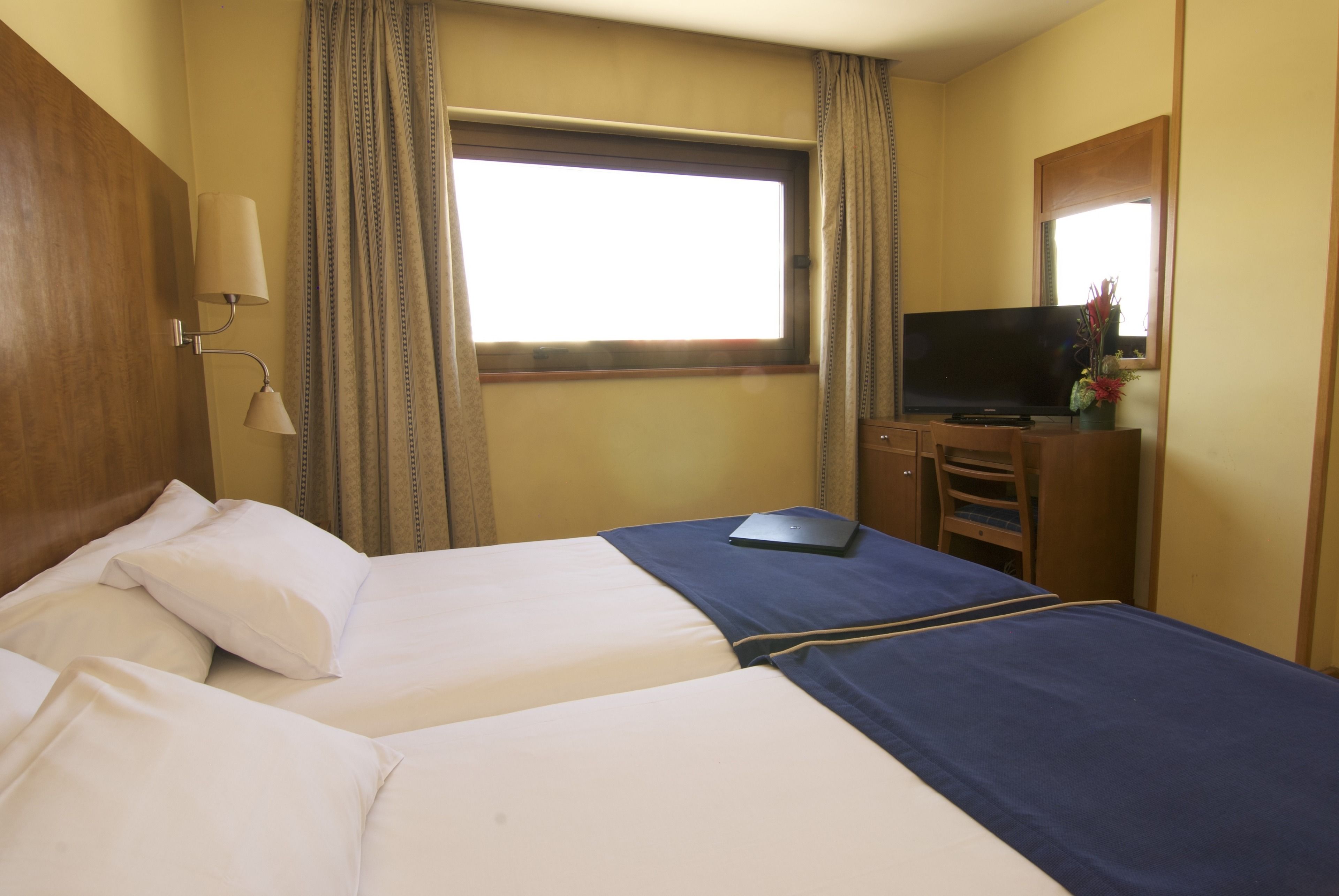 A hotel room with two beds, a television, a laptop, and a window with curtains.