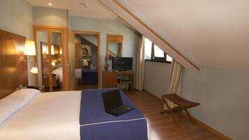 Habitación de hotel con cama, laptop, escritorio con silla, televisor y ventana con cortinas.
