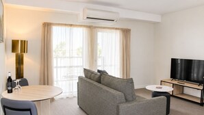 A modern hotel room with a sofa, a dining table, a TV, and an air conditioning unit. - Quest Mildura (Mildura)