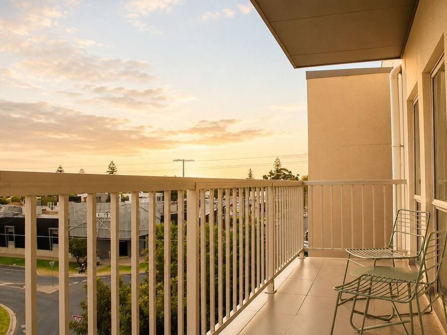 A balcony with a view of a road and buildings, metal chairs, and a building with a beige facade.