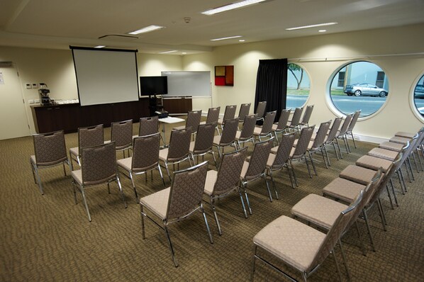 A conference room with rows of chairs, a projector screen, a whiteboard, and a window with a view of a street. - Quest Mildura (Mildura)