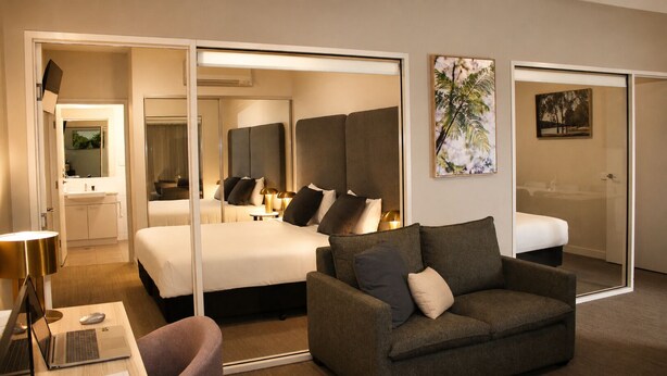 A hotel room with a bed, a sofa, a desk with a laptop, a mirror, and artwork on the walls. - Quest Mildura (Mildura)