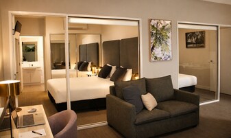 Una habitación de hotel con una cama, un sofá, un escritorio con una computadora portátil, un espejo y obras de arte en las paredes.