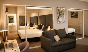 A hotel room with a bed, a sofa, a desk with a laptop, a mirror, and artwork on the walls. - Quest Mildura (Mildura)