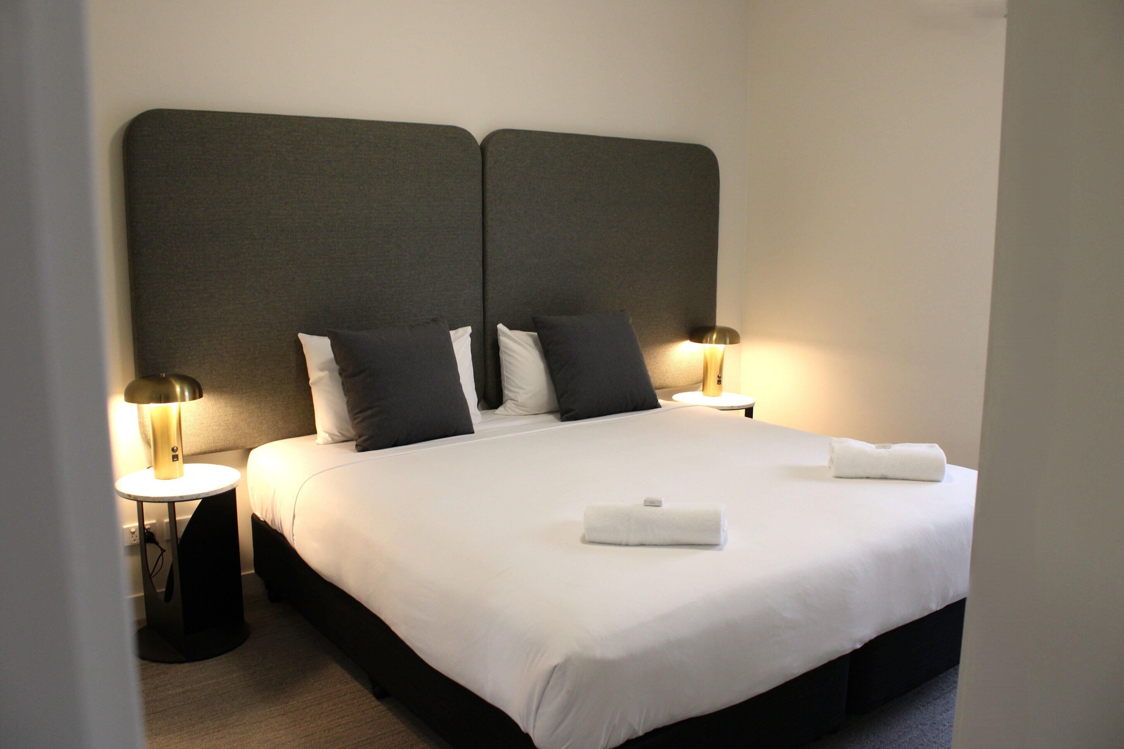 A neatly made bed with white linens, two bedside lamps, and a dark headboard.