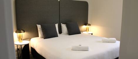 A neatly made bed with white linens, two bedside lamps, and a dark headboard.
