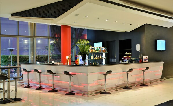 A modern bar area with a long counter, multiple stools, and a large window providing a view of the outdoors.