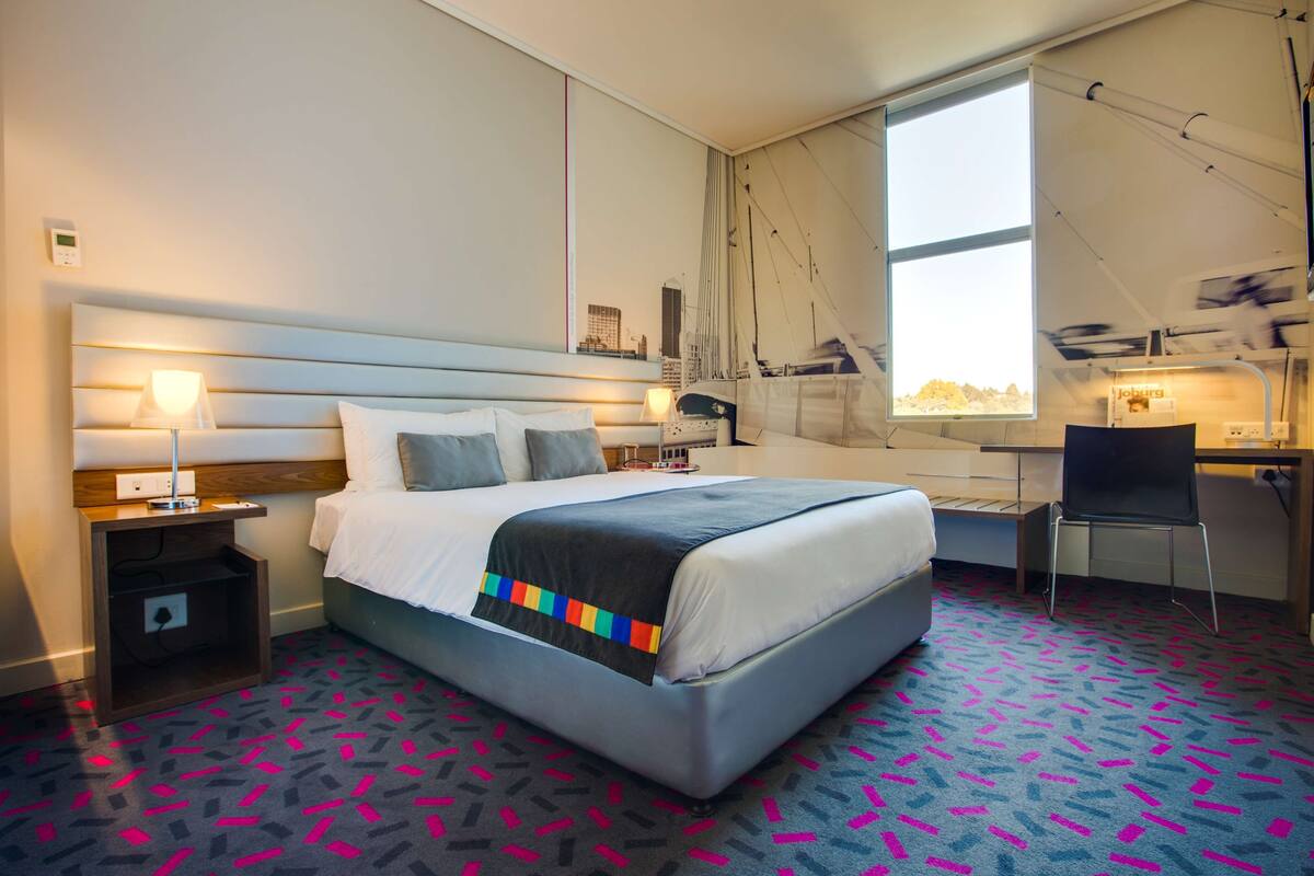 Una habitación de hotel con una cama, mesitas de noche, un escritorio y una silla.