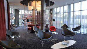 Eine moderne Hotelhalle mit einer zentralen Wendeltreppe, schwarzen und roten Stühlen sowie großen Fenstern.