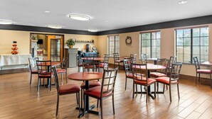 A spacious dining area with round tables and chairs, a kitchen in the background, and large windows with blinds. - Best Western Moriarty Heritage Inn (Moriarty)