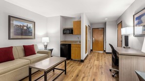 A compact hotel room with a kitchenette, a sofa with red cushions, a dining table, and a desk with a lamp. - Best Western Moriarty Heritage Inn (Moriarty)