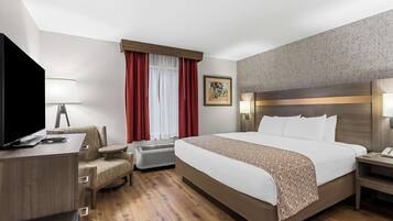 Quarto de hotel com uma cama grande, uma escrivaninha com cadeira, televisão e janela com cortinas vermelhas.
