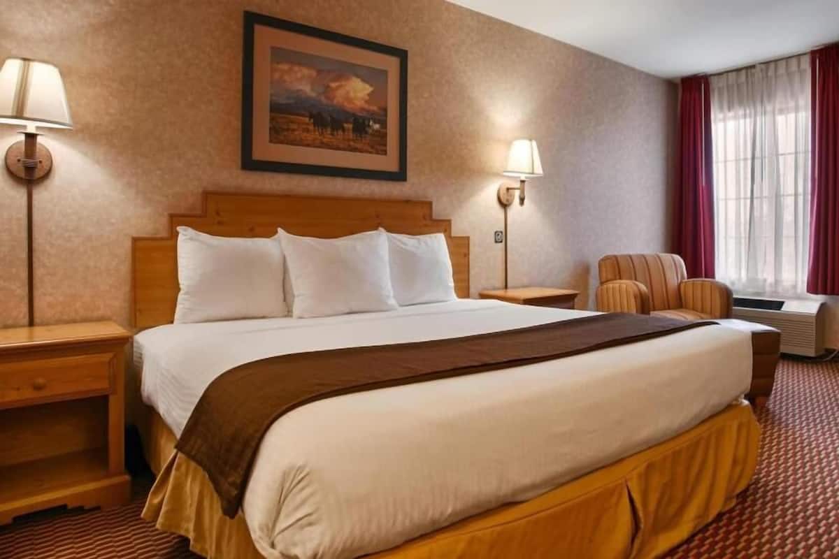 A hotel room with a large bed, two bedside tables, a chair, a painting on the wall, and a window with curtains.