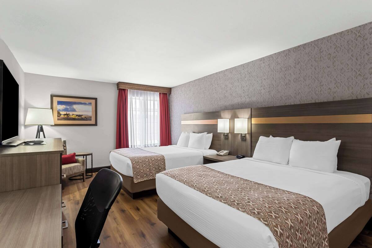 A hotel room with two beds, a desk with a lamp, a chair, a TV, and a painting on the wall.