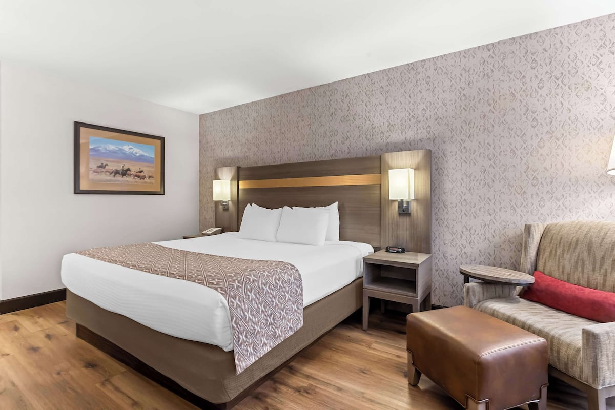 A hotel room with a large bed, bedside tables, a chair, and a small table.
