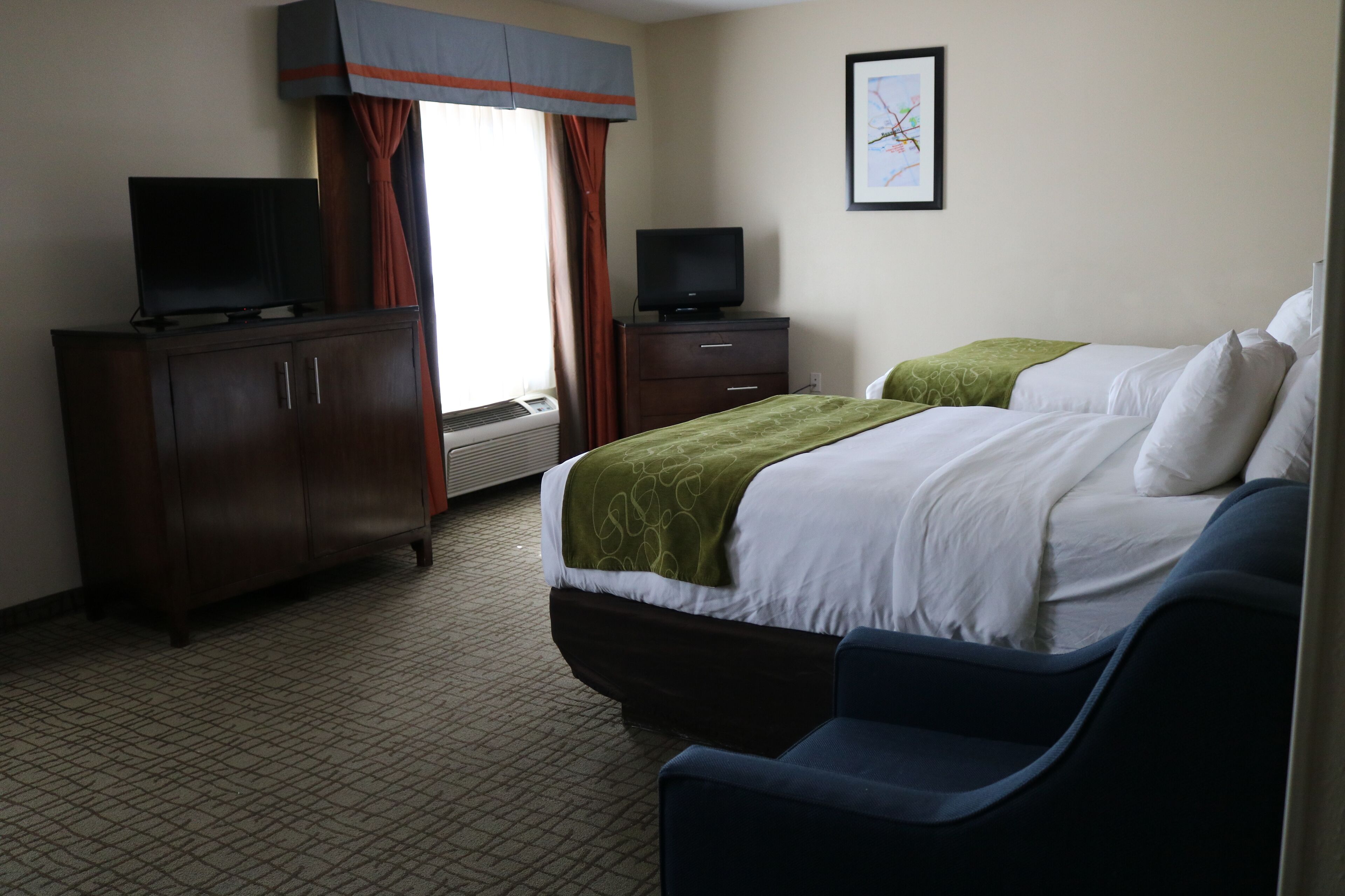 A hotel room with two beds, a TV on a cabinet, and a framed picture on the wall.