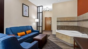 A hotel room with a blue sofa, a small table, a bathtub, and a door leading to another room. - Comfort Suites Roswell North (Roswell)