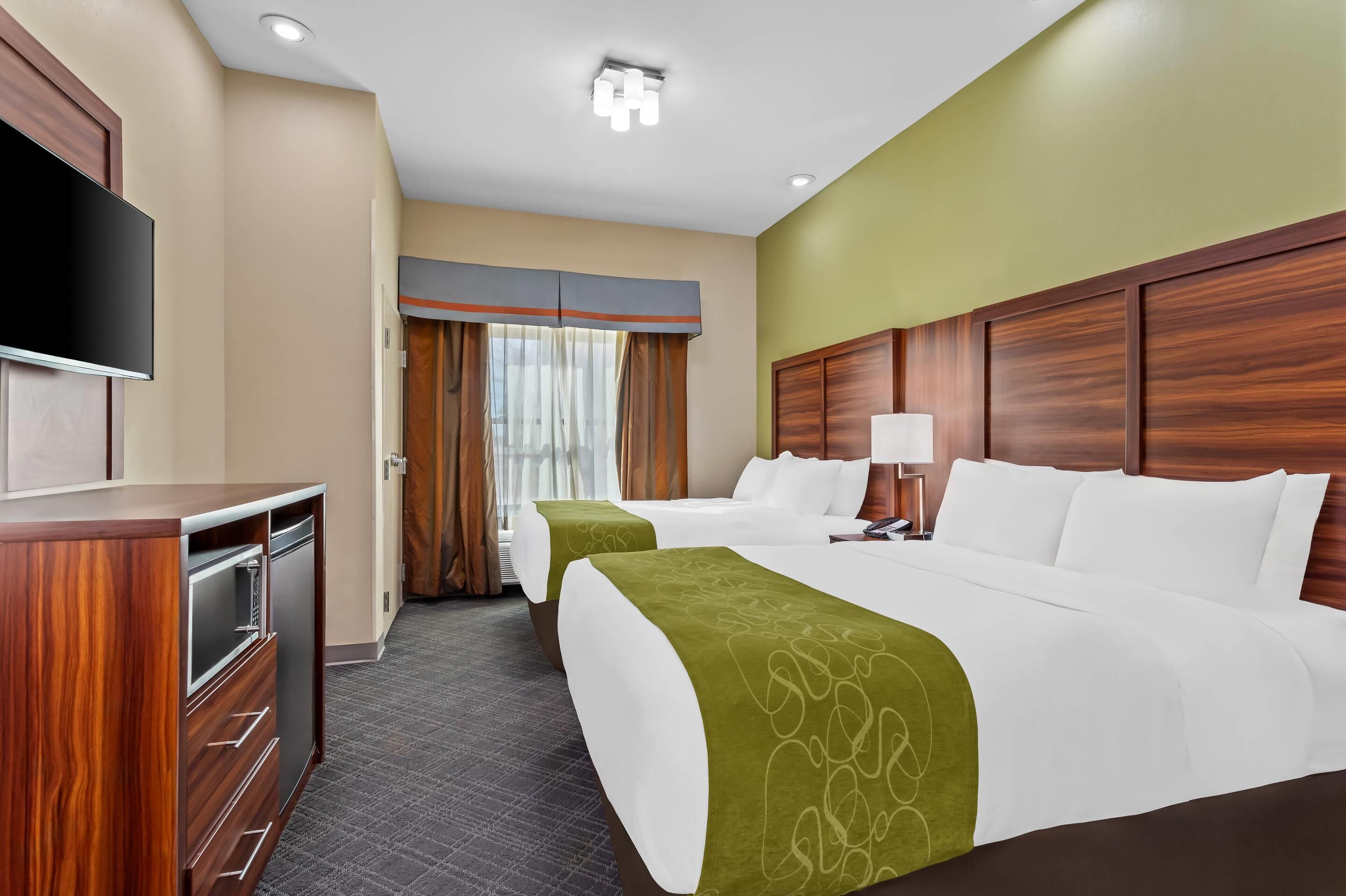 Una habitación de hotel con dos camas, televisor, escritorio y ventana con cortinas.