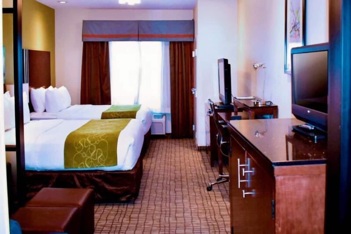 A hotel room with two beds, a desk with a TV, and a window with curtains.