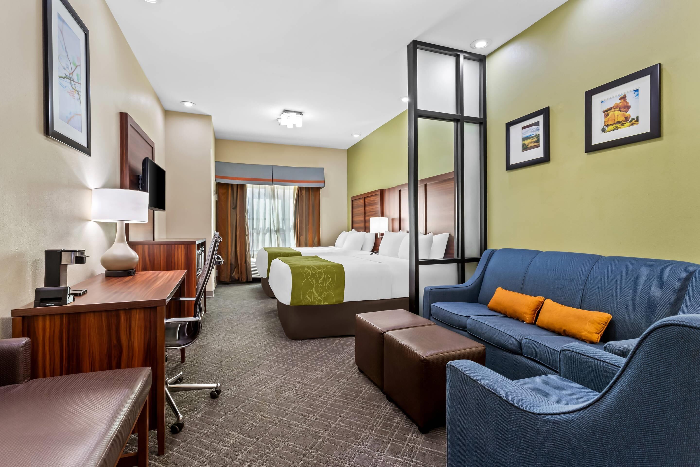 A hotel room with a bed, a blue sofa, a desk with a lamp, and a TV.
