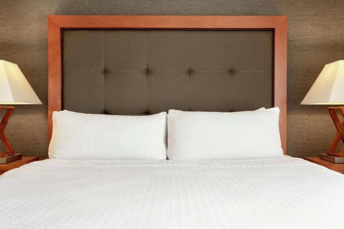 Ein Bett mit einem gepolsterten Kopfteil, zwei Nachttischlampen und einer weißen Bettdecke mit Struktur.