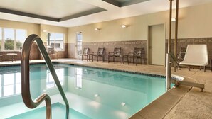 A swimming pool with a metal ladder, lounge chairs, and a tiled wall.