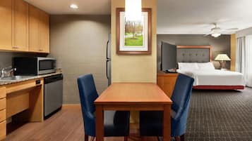 Une chambre d’hôtel comprenant une table à manger en bois, deux chaises, un lit, une télévision, un four à micro-ondes et un réfrigérateur.