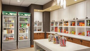 A hotel pantry with shelves stocked with snacks and beverages, and two refrigerators labeled "Homewood Suites."