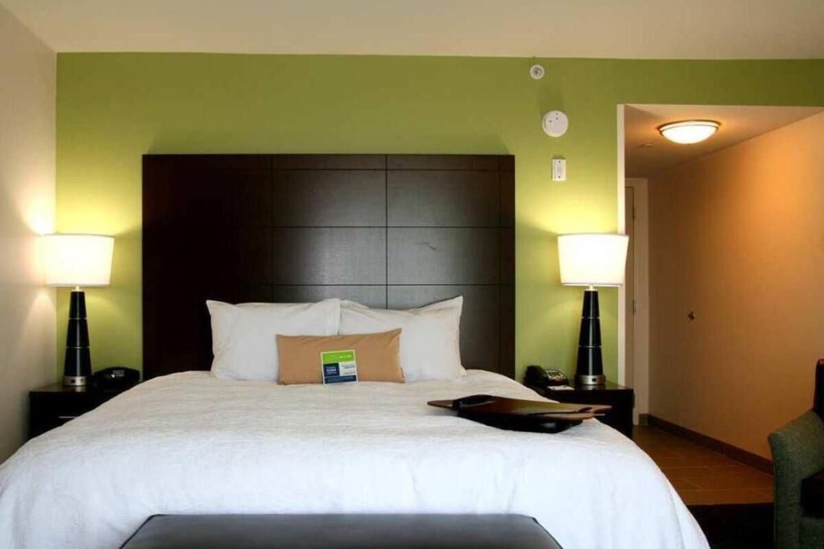 A hotel room with a large bed, two bedside lamps, a nightstand, a bedside table, and a green wall.