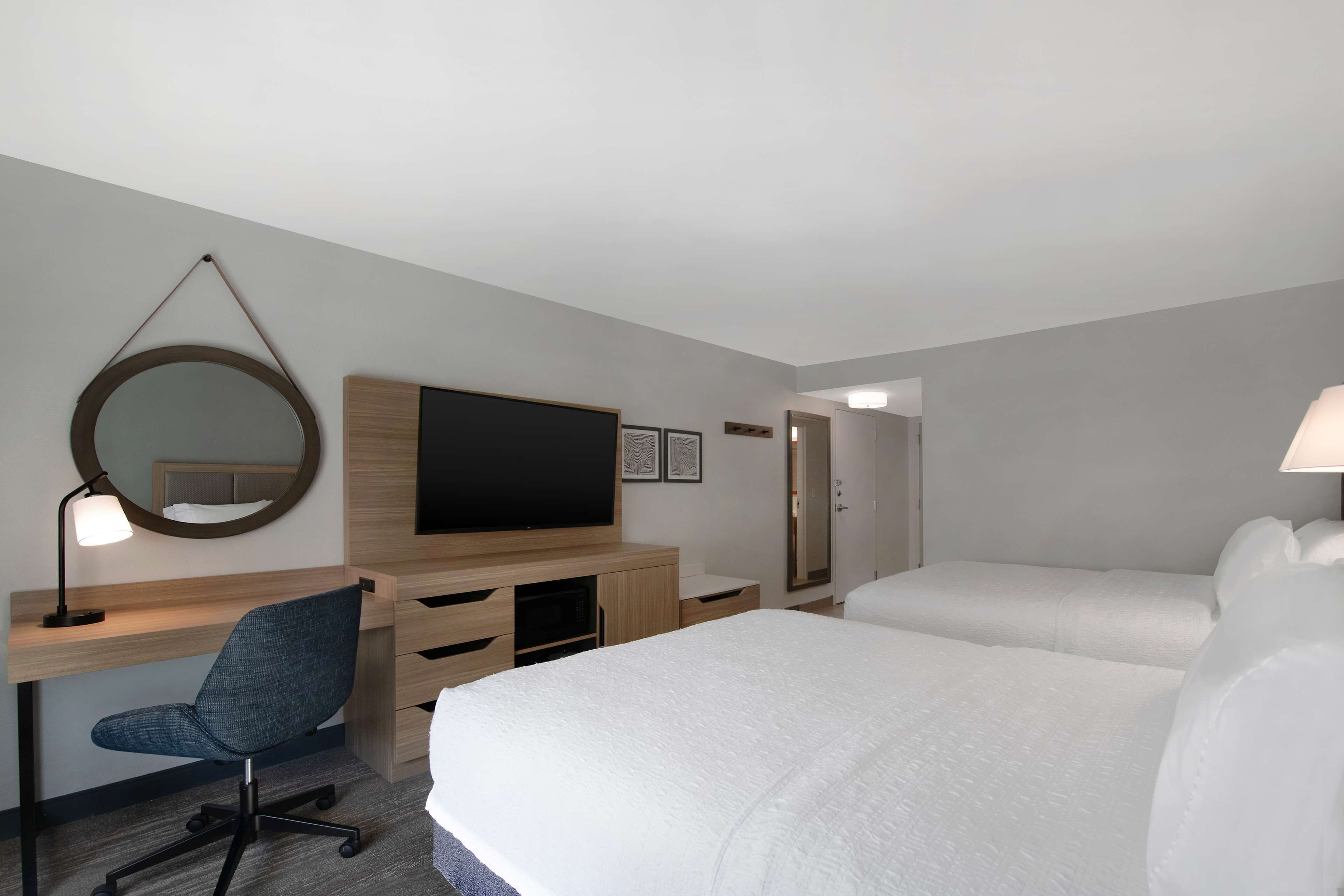 A hotel room with a desk, chair, TV, two beds, and a mirror.