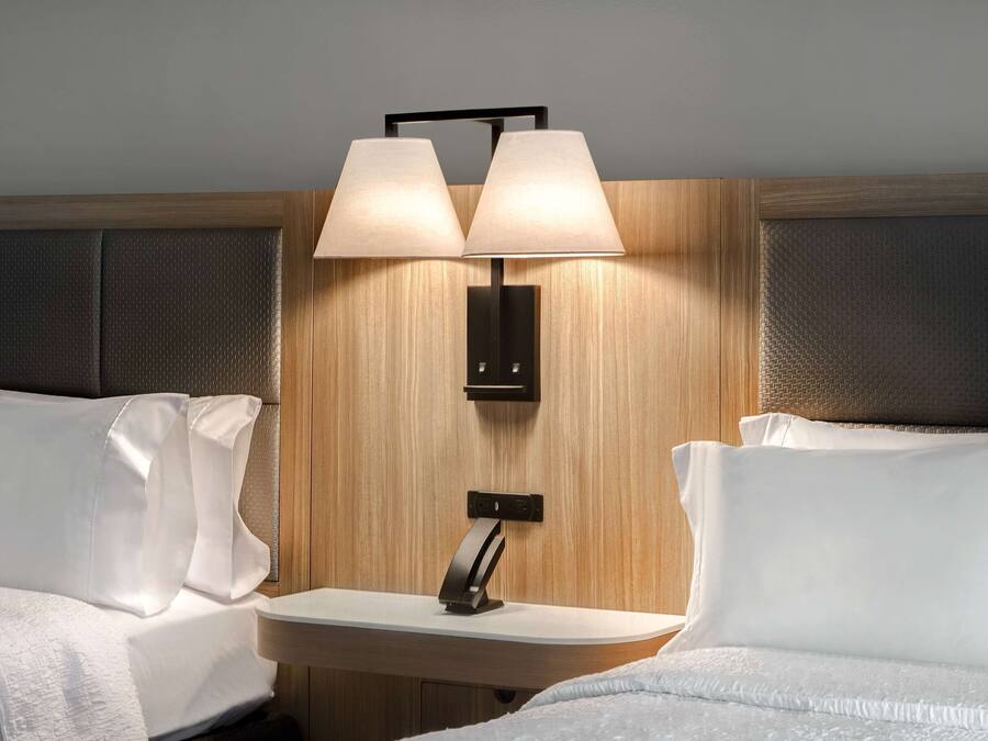 Una camera d'albergo con due letti, un comodino e una lampada fissata alla parete.