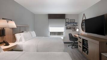 A hotel room with two beds, a desk, a television, and a window.