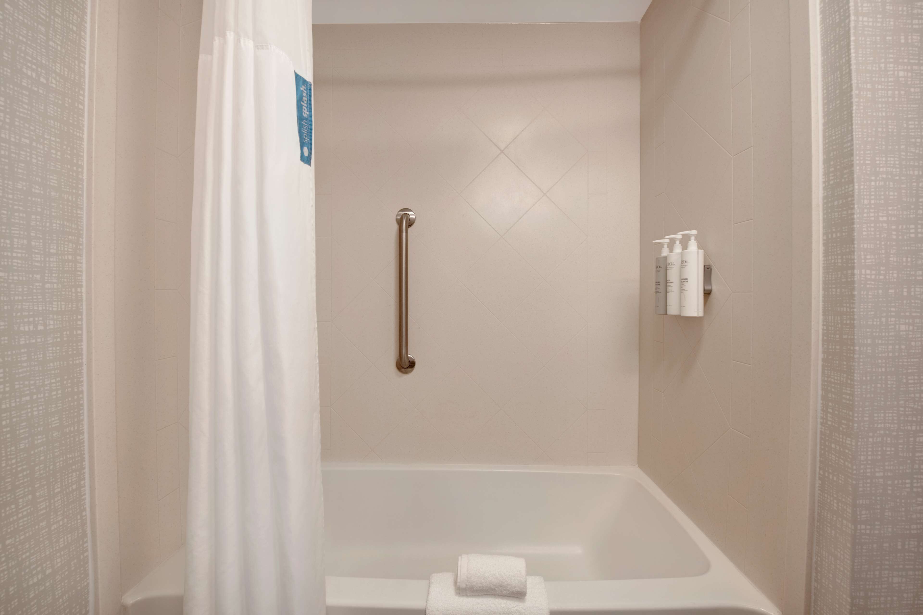 A bathroom with a bathtub, a handrail, and a towel rack with toiletries.
