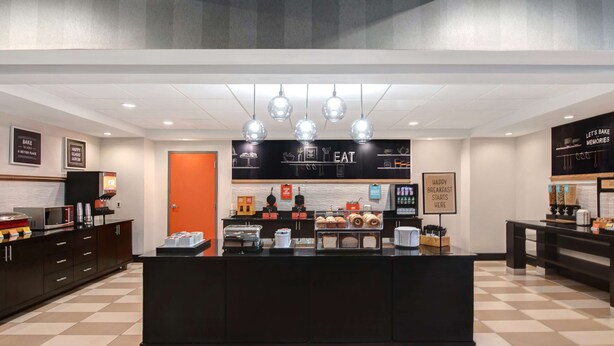A modern breakfast area with a checkered floor, a central counter with food displays, and a sign that reads "Let's Bake Memories." - Hampton Inn Anderson/ Alliance Business Park (Anderson)