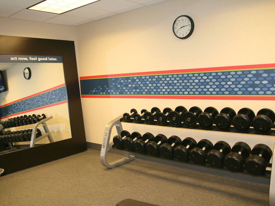 Un gimnasio con un reloj de pared, una frase motivacional y un estante con mancuernas.